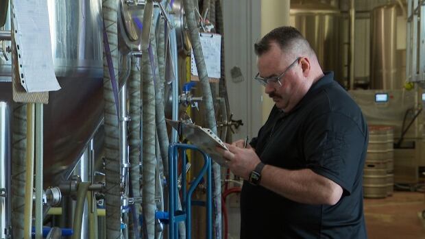 Dave McGuire of Bogside Brewing in Montague, P.E.I. A man looks down at a clipboard and takes notes with beer vats in the background.
