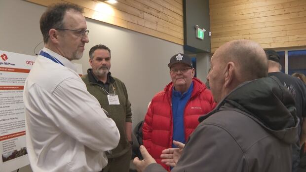 Willie Spence (right) says he needs home dialysis and was frustrated by the inaccuracy of estimated restoration times. Four men stand in a circle. The man on the right, wearing a grey jacket, is speaking with his hands raised to chest-height.