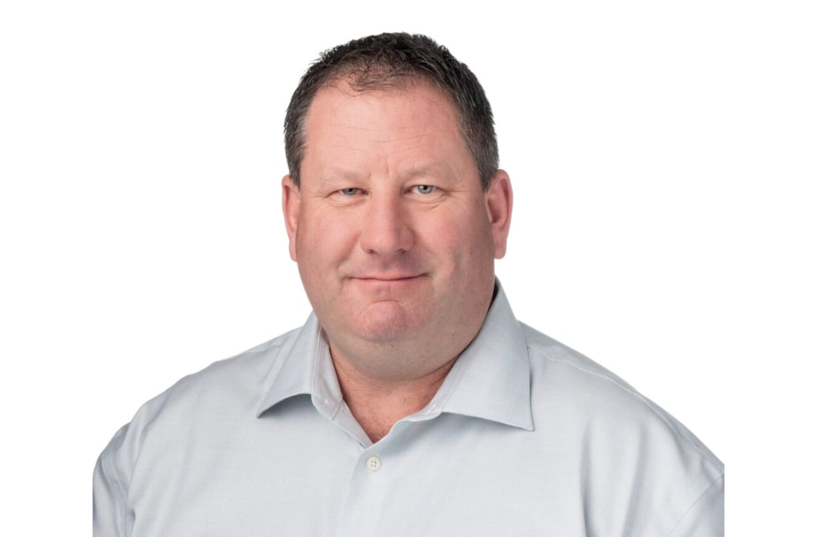 A man with short hair smiles wearing a white shirt with a white background.