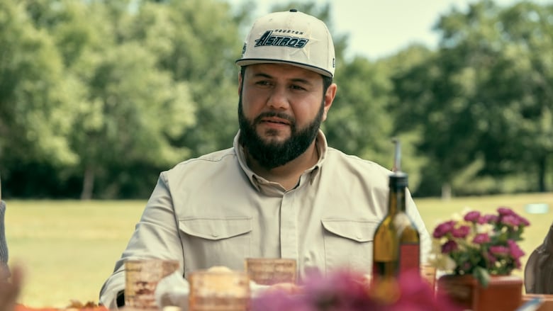 A man sits outside at a picnic table with a baseball hat on.