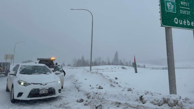 A photo from Thursday's storm shows poor travel conditions between Edmundston and Fredericton. On Friday, some highways are still snow-covered. A car parked on the side of the road with blowing snow around.