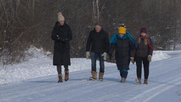 Steven Bell has been bringing his two daughters to the property since they were young. They spend their time in the wilderness identifying plants and picking mushrooms 4 people walk side by side down a snow covered highway with a forest in the background