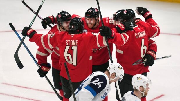 Connor McDavid, back centre, celebrates with teammates after opening the scoring during a win over Finland at the 4 Nations Face-Off on Monday at TD Garden in Boston. A group of ice hockey players wrap their arms around each other in celebration as two opposing players skate away.