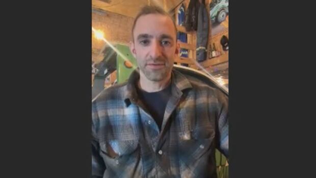 Nick Haddad, the owner of Nick's Towing, A man stands wearing a grey, white and blue plaid button-up shirt.