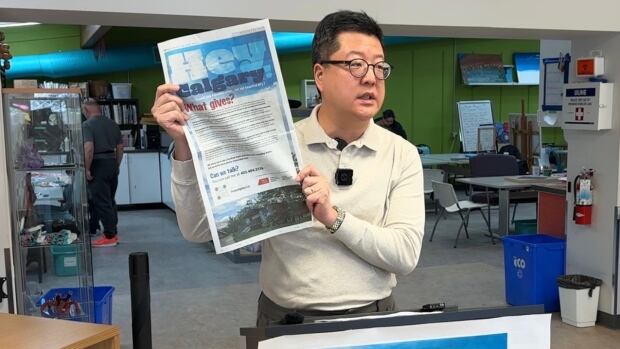 The National accessARTS Centre CEO Jung-Suk Ryu holds up a a full-page newspaper ad calling on the city to work with the disability arts organization on relocating it out of the Fairview Arena. A man holds a newspaper.