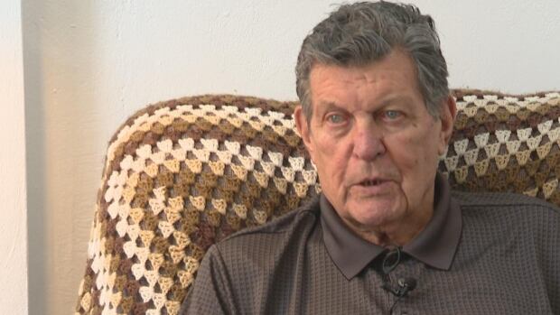 Ossie Gildart was told his licence was suspended until he pays $4,661.91 because he'd had an uninsured accident — an accident that happened in Toronto in 1960. An older man is sitting on an afghan-covered chair.