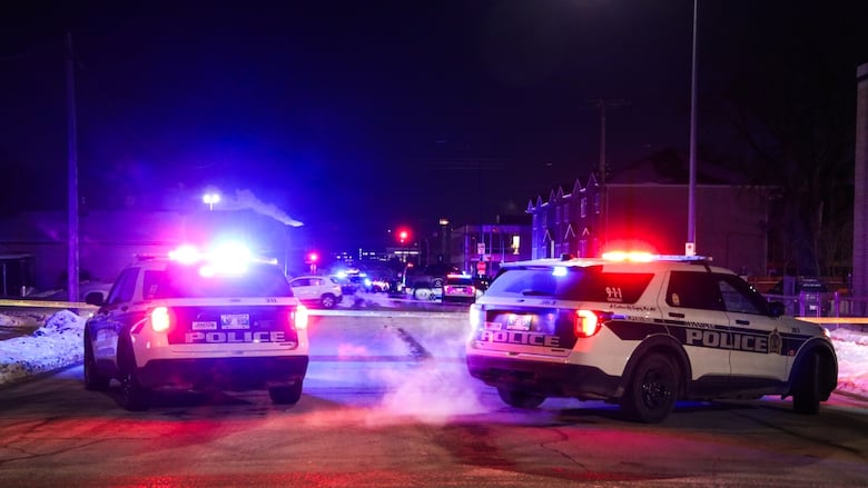 Two police cruisers with lights on are in the foreground of a nighttime photo with other police vehicles in the distance