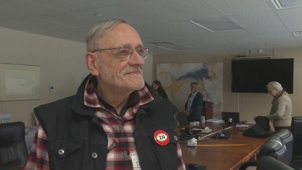 Paul Henry Leblanc says he goes to the nursing home where his father lives almost every day to make sure he gets out of his wheelchair and goes for a walk. A man in a checkered shirt and black vest stands in a classroom.