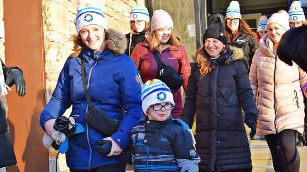 Crowds of people will descend on six New Brunswick municipalities on Saturday for Coldest Night of the Year events. Three of the municipalities had surpassed their fundraising goals as of Friday, including the Fredericton walk, pictured here in 2024. A group of smiling people wearing white and blue toques walking out of an entryway