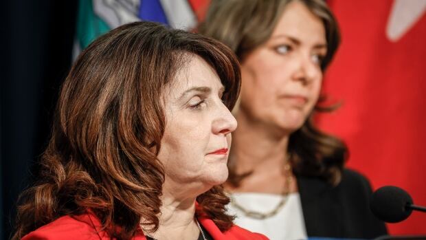 Alberta Premier Danielle Smith, right, and Minister of Health Adriana LaGrange provide an update on what steps the government is taking related to allegations by former Alberta Health Services CEO Athana Mentzelopoulos, in Calgary, Alta., Wednesday, Feb. 19, 2025.THE CANADIAN PRESS/Jeff McIntosh Close-up: a woman stares rightward as another woman behind her gazes in same direction