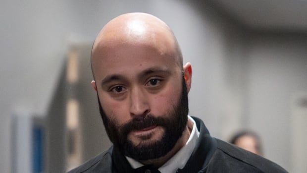 A man with a bald head and a full beard looks straight ahead.