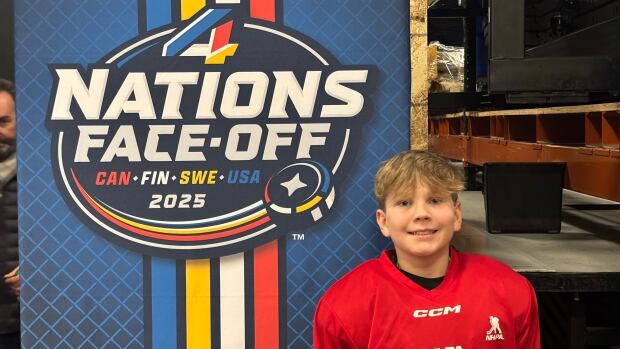 Ryan Evans cheered and clapped as team Canada won the 4 Nations Face-Off finals against team U.S.A on Thursday. A white boy with blonde hair, standing next to a hockey banner wearing red coloured hockey uniform.
