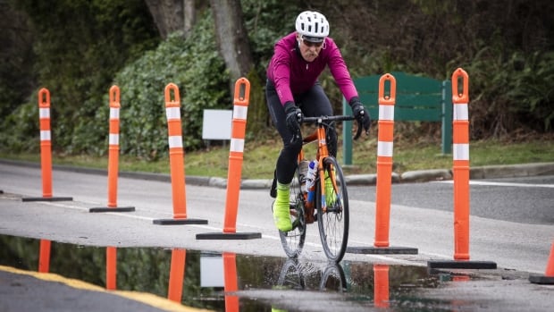 A biker wearing a pink top rides through a puddle on a bike lane marked with orange emergency markers.