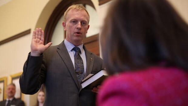 Martin Long was sworn in as infrastructure minister on Thursday. A man in a suit holds a book and hold up his hand at a swearing-in ceremony.
