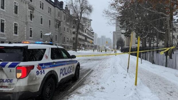 An Ottawa Police Service vehicle is parked on Laurier Avenue E. on March 1, 2025. Police say a man in his 20s suffered life-threatening injuries after being hit by a vehicle that morning. A police vehicle is parked on a snowy city road, with yellow police tape strung up next to it.