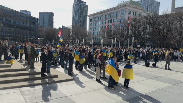 Calgary's Ukrainian community rallied on Sunday after a tense exchange between the leaders of Ukraine and the United States. A group of people draped in blue and yellow Ukrainian flags holding signs.