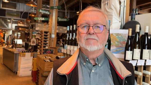 Richard Harvey, co-owner and founder at Metro Vino, says the new measures are taxation by another name. a beared grey haired man in glasses standing amongst wine bottles on shelves