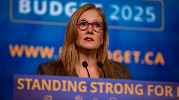 A woman stands at a podium in front of a blue background that says Budget 2025.