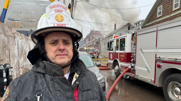 Firefighter stands near a firetruck wearing firefighting attire.