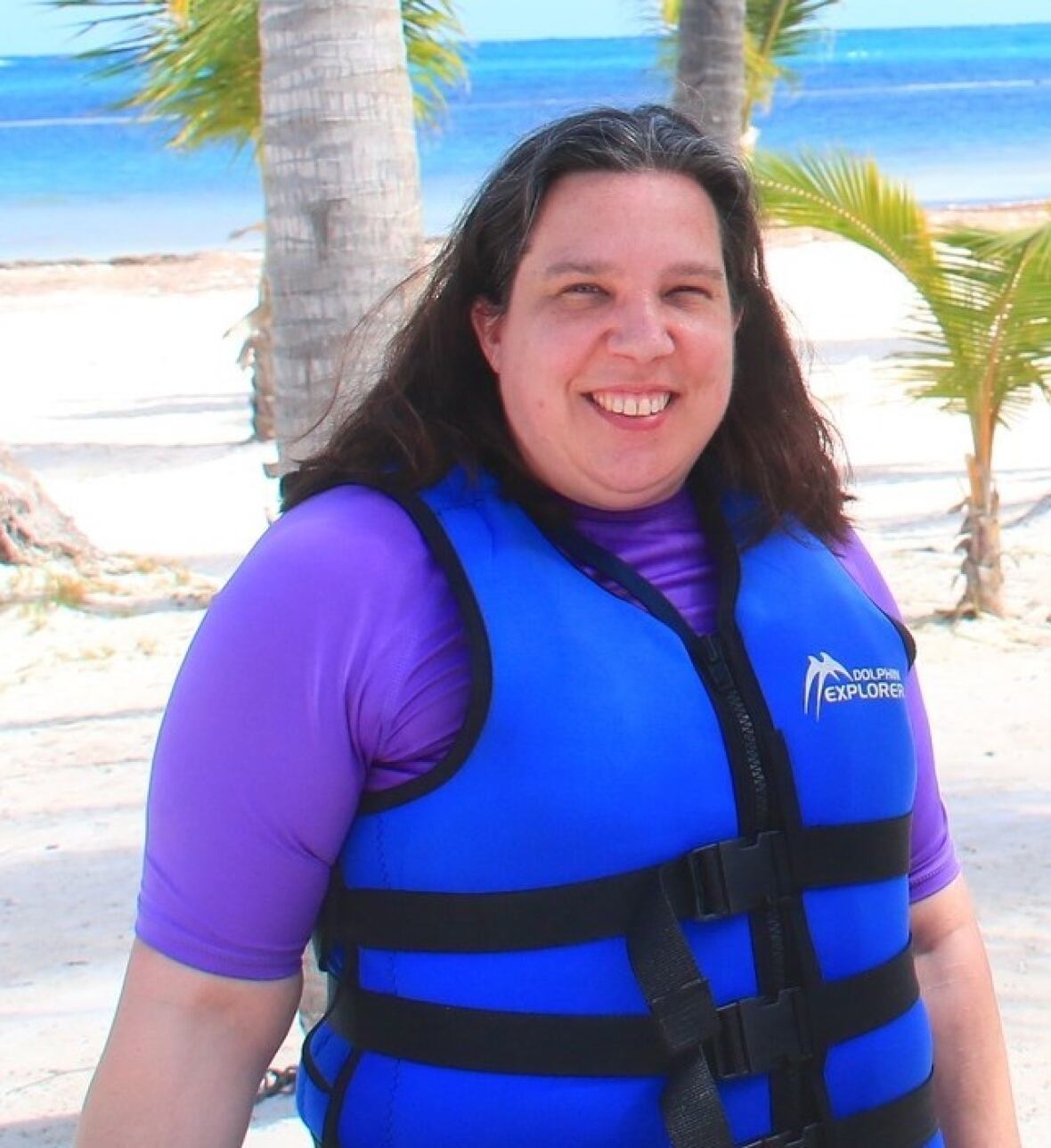Woman wearing a lifejacket smiles portion    posing connected  a sandy tropical beach.