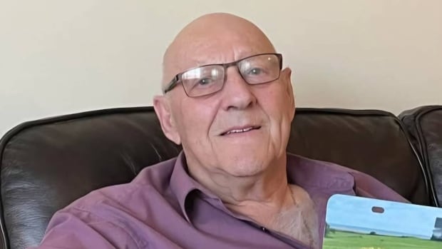 Elmer Arsenault is described as five feet 10 inches tall, 220 pounds with short grey hair and green eyes. A man sitting in a living room. He is looking at the camera.