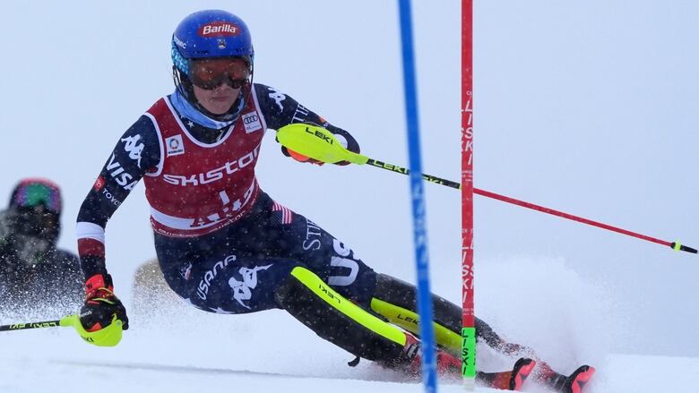 A pistillate  alpine skier leans to her close    arsenic  she speeds down   a slalom course.