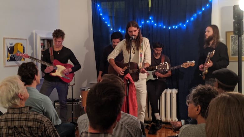 Five men play music for an audience in a living room.