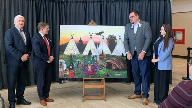 From left: Indigenous Affairs and Reconciliation Minister Scott Reid, Premier Andrew Furey, Miawpukek First Nation Chief Bradley Benoit and Conne River Artist Brittany Wiseman reveal Wiseman's painting, Powwow Serenity. Four people stand around a painting showing a powwow.