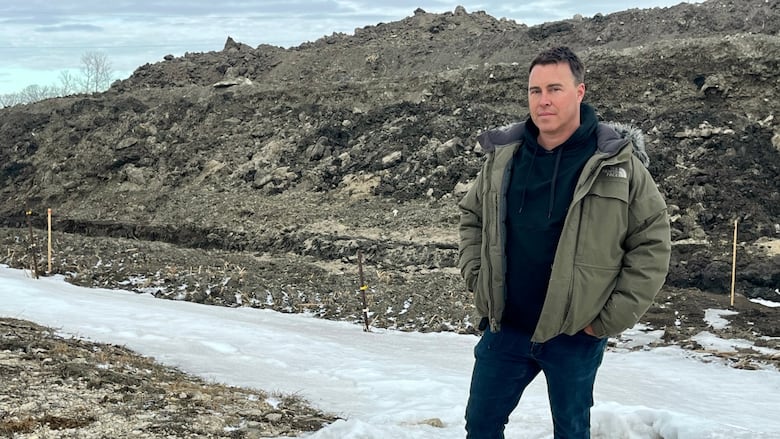 A man standing before a frozen ditch and a large mound of earth.