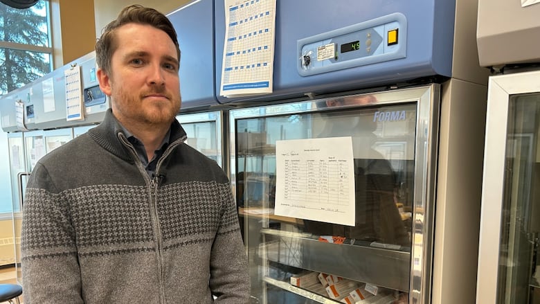 A man stands in front of a vaccine fridge.
