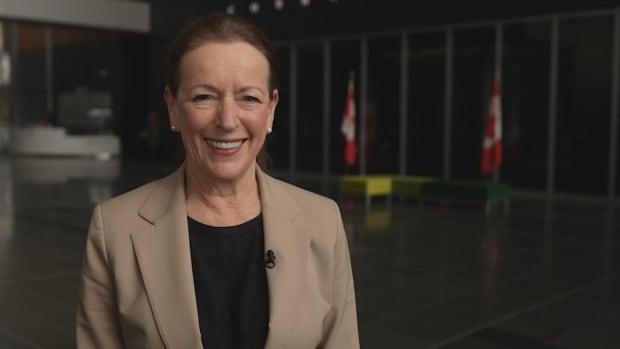 A white woman wearing a light brown coat smiles.