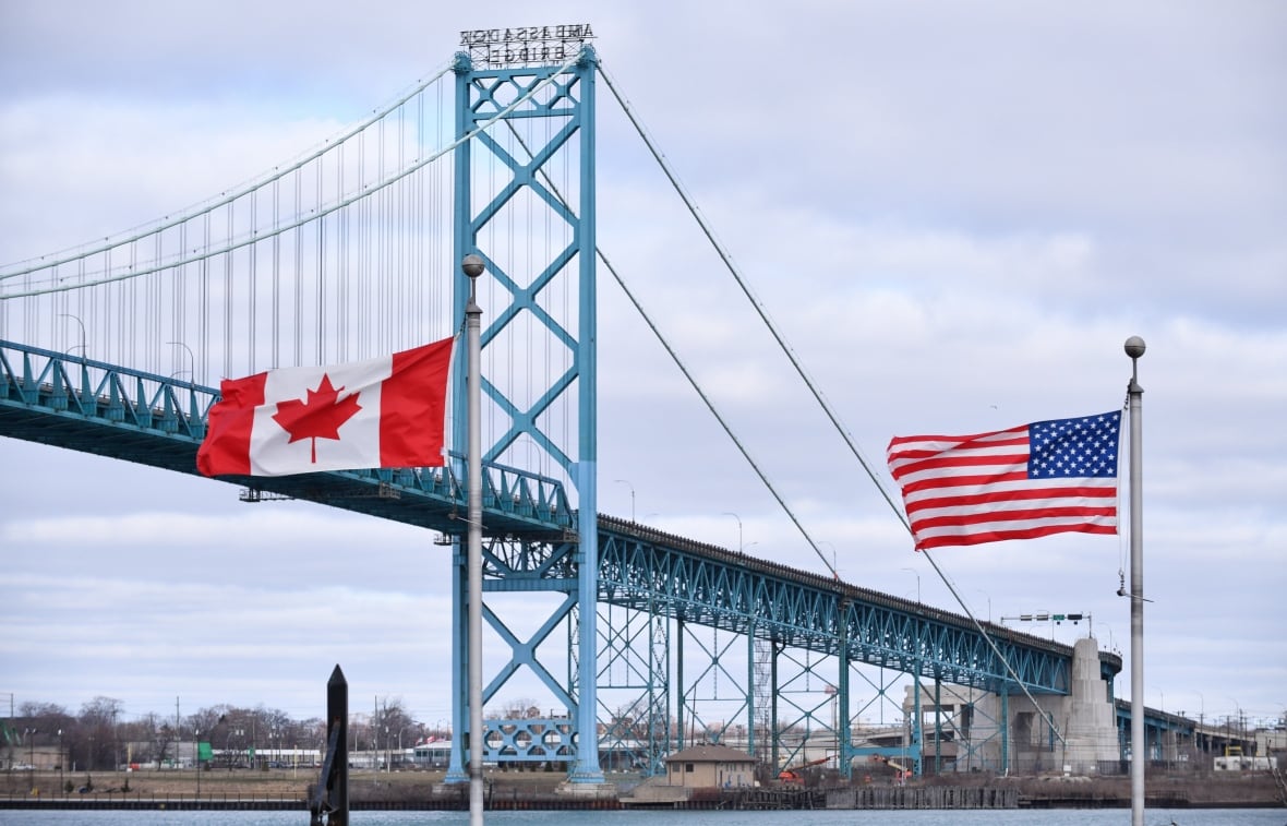 Two flags sit near each other by a bridge that connects Canada to the United States.