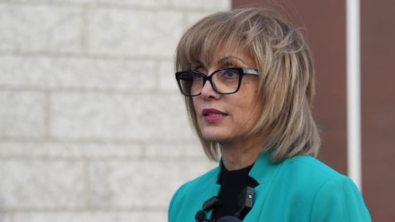 A woman wearing glasses and a turquoise jacket.