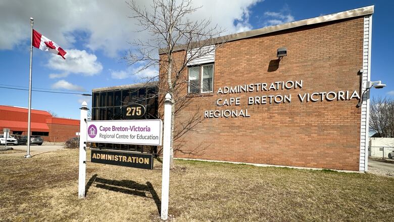 A reddish  ceramic  gathering  is shown with brownish  grass, bluish  entity  and a red-and-white Canadian emblem  flying and a motion   saying Cape Breton-Victoria Regional Centre for Education administration.
