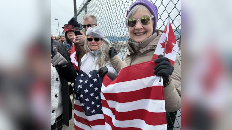 People are seen lasting  against a chain-link fence, holding Canadian and American flags.