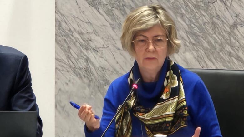 Woman sitting astatine  podium speaking into microphone.
