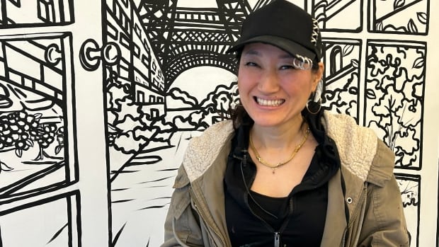 Ji Hyang Ryu is the Moncton-area artist who decorated every wall at Riverview's Tambayan Café. A chinese lady wearing a black hat and beige coat. She is standing in front of a wall with black and white drawings on it.