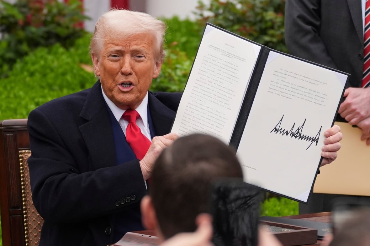 A man with white hair holds up a document to a crowd. 