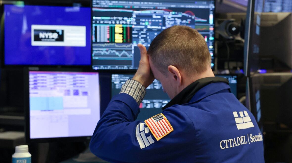 A man, sitting in front of several computer monitors, puts his hand to his forehead, as if in exasperation.