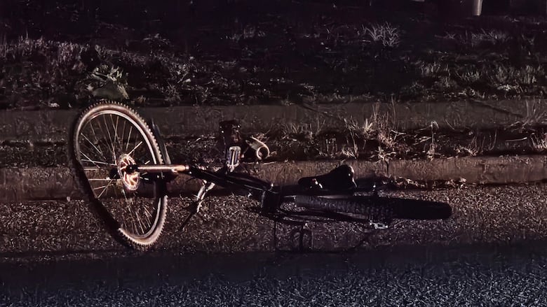 A bicycle with a bent wheel is seen laying on a road.