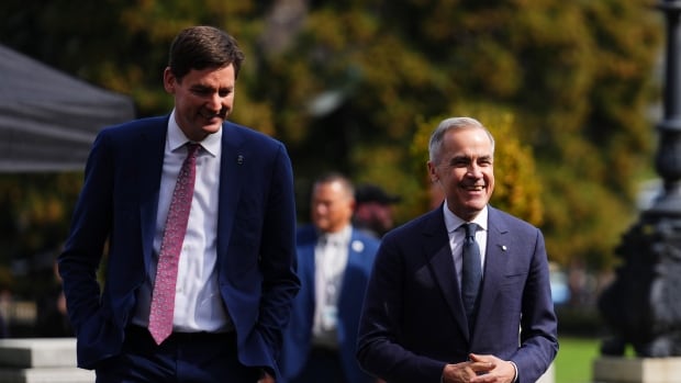 Two men wearing suits smile as they walk outdoors.
