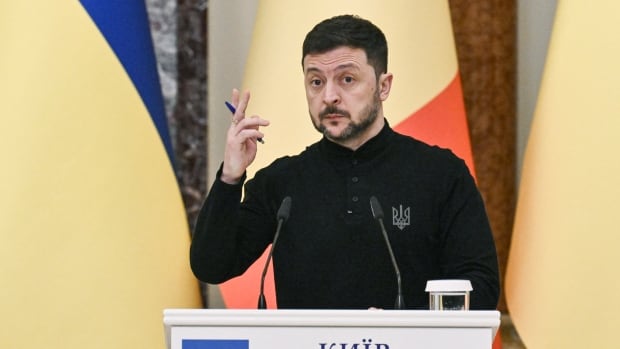 A bearded dark haired man is shown speaking at a podium.
