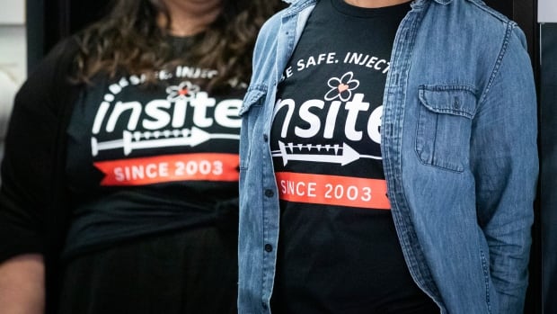 Two women wear black T-shirts that read 'Be Safe. Inject Insite since 2003'.