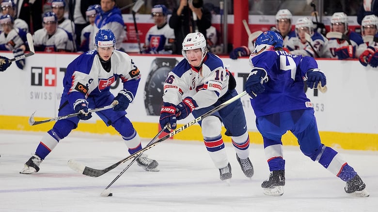 A player in white carries the puck between two opponents in blue.