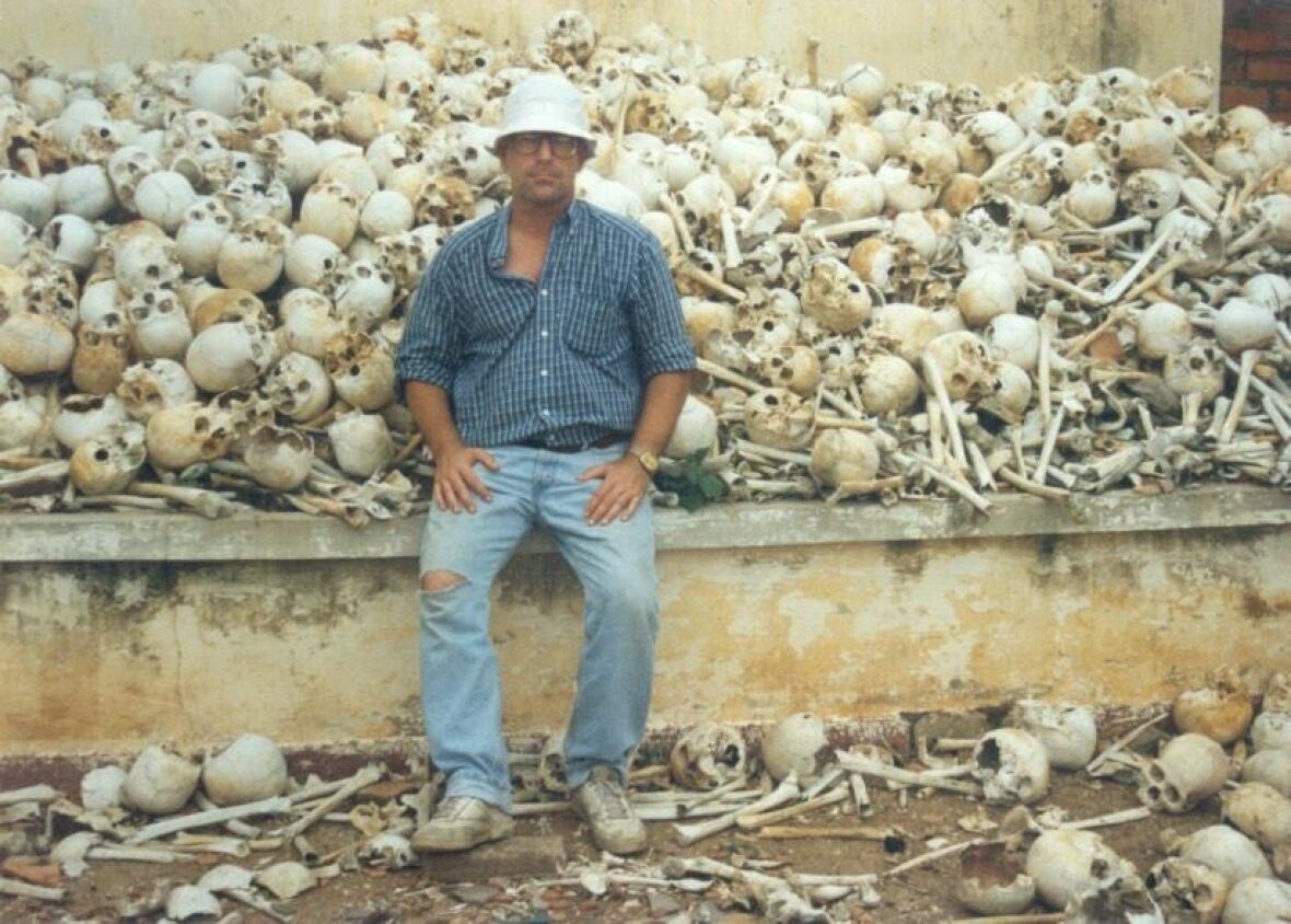 Um homem fica à beira de uma cena em ruínas, na beira de um crânio e na borda da montanha osso e derramou no chão.