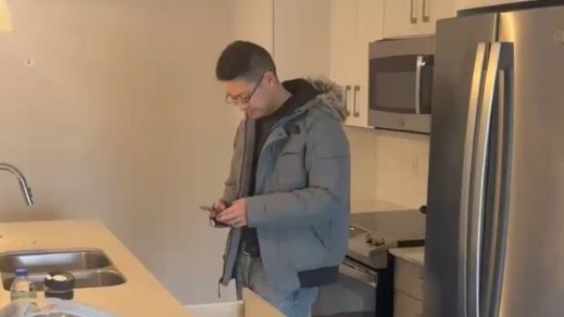 A man stands in a kitchen looking down at his phone.