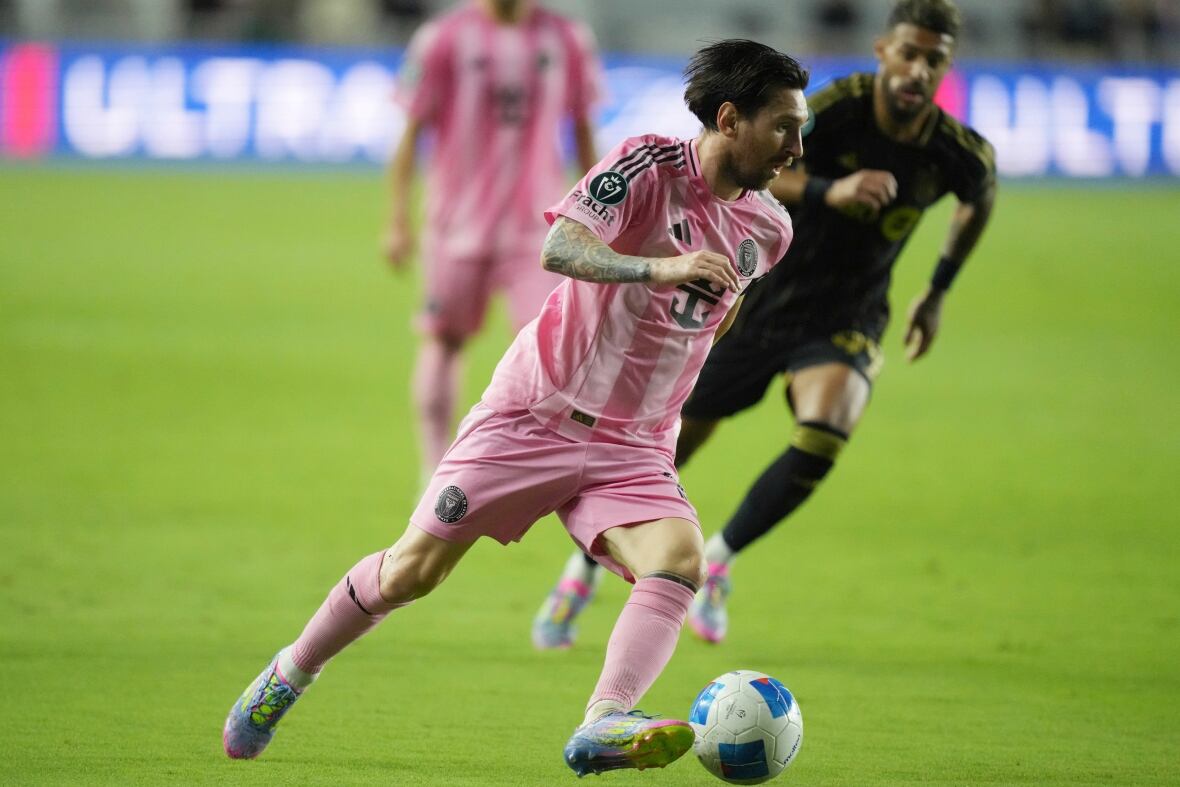 Lionel Messi, dressed in light pink soccer equipment, handles a soccer ball on a field.