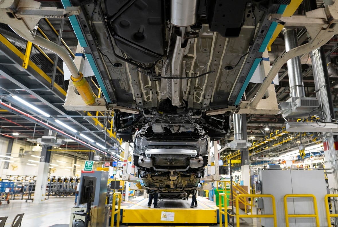 An auto assembly line and plant is shown, showing the undercarriage of a vehicle which has been hoisted in the air.
