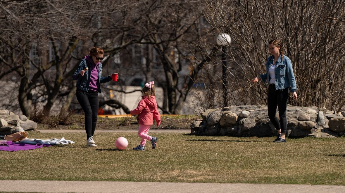 See women and child playing with ball in park.