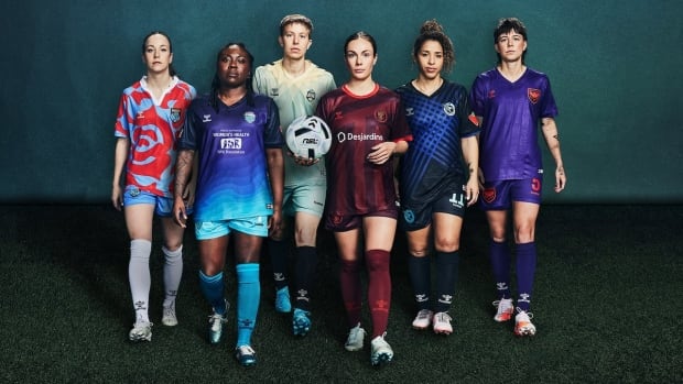 Six female soccer players pose alongside each other during a photo shoot on turf.